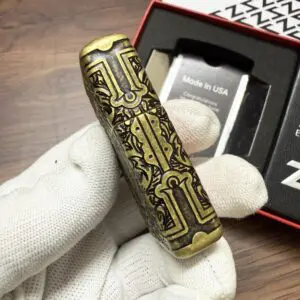 29719Asia_01 Ornate brass cylinder with intricate black engraving held by a gloved hand, packaging in the background reading 'Made in USA'.