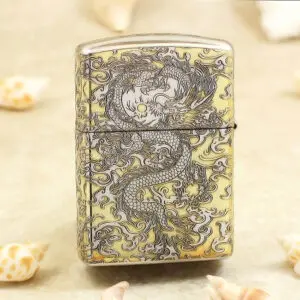 Metal lighter with an intricate dragon engraving in dark lines on a gold-tone surface.