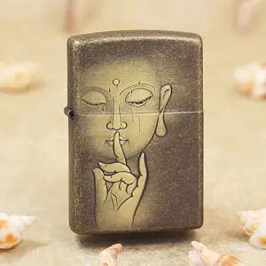 Bronze metal lighter with a line drawing of a person holding a finger to their lips, signaling 'shh', on a sandy surface with seashells nearby.