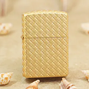 Gold woven-pattern lighter standing on sand with small seashells around it.