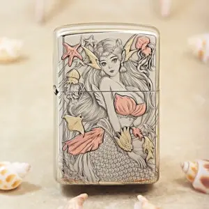 Metal lighter with a detailed mermaid illustration in pale pink and gold tones, other sea motifs around her.
