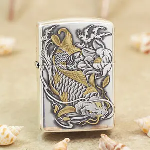 Metallic lighter with a raised gold-and-silver koi fish design, surrounded by waves and flowers on a sandy surface.