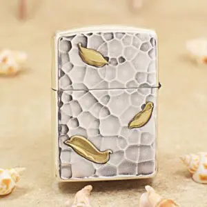 KZ148-01 Metallic lighter with a textured, pebble-like surface and gold leaf accents on a sandy background.