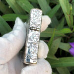 Close side view of the hinge and arabesque engraving on the sterling silver Zippo Armor lighter