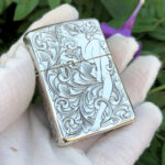 Hand-held front view of the reclining woman and scrollwork on the sterling silver Zippo Armor lighter