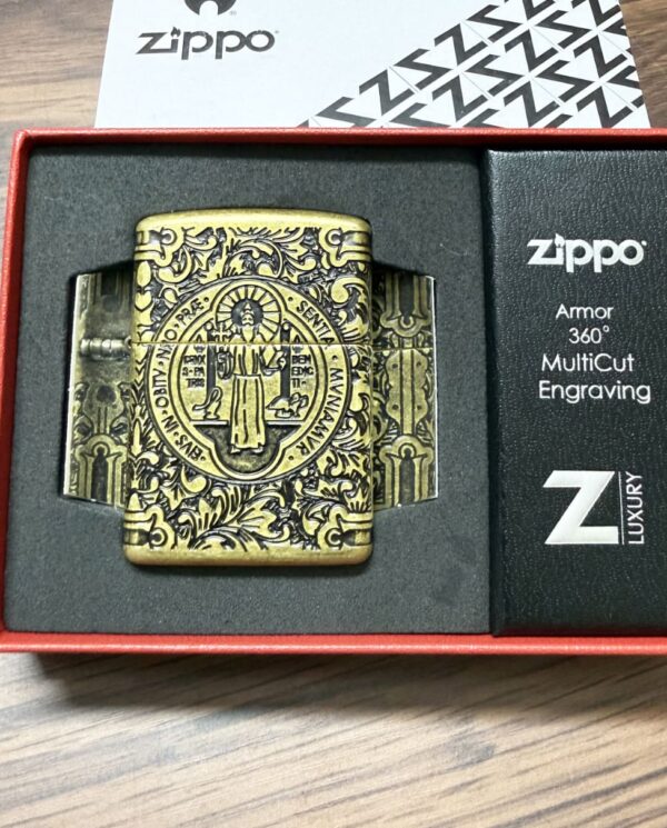 Brass Zippo lighter with ornate engraving in a black foam insert of a red gift box, showing circular crest and detailed scrollwork