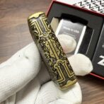 Ornate brass cylinder with intricate black engraving held by a gloved hand, packaging in the background reading 'Made in USA'.