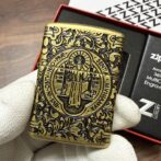 Brass ornate lighter with a circular religious medallion and floral engravings, held by a gloved hand.