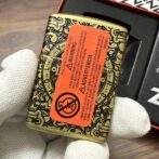 Ornate gold-and-black metal tin with an orange warning label held by gloved hands