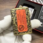 Ornate brass tin with a red warning label being held by gloved hands; decorative engraving on the container.