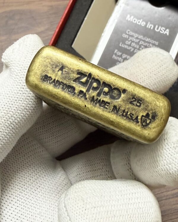 Brass Zippo lighter stamped 'Made in USA, Bradford, PA' held by gloved hand.