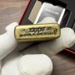 Gold Zippo lighter held in white-gloved hand, engraved with Made in USA and Bradford, PA.