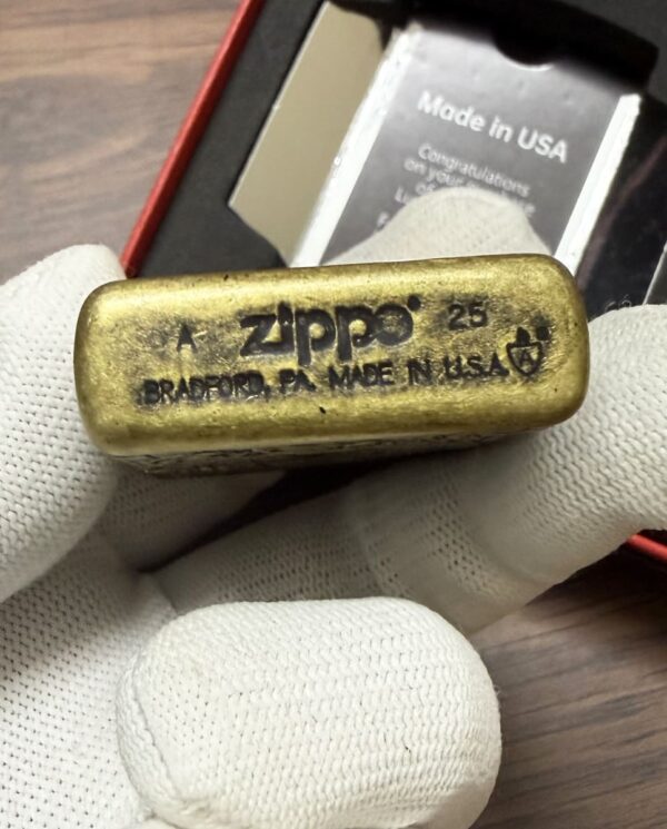Gold Zippo lighter held in white-gloved hand, engraved with Made in USA and Bradford, PA.