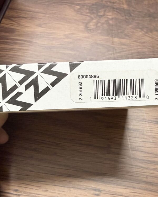 White cardboard box with black geometric pattern, held by hand, showing a barcode sticker on the side.