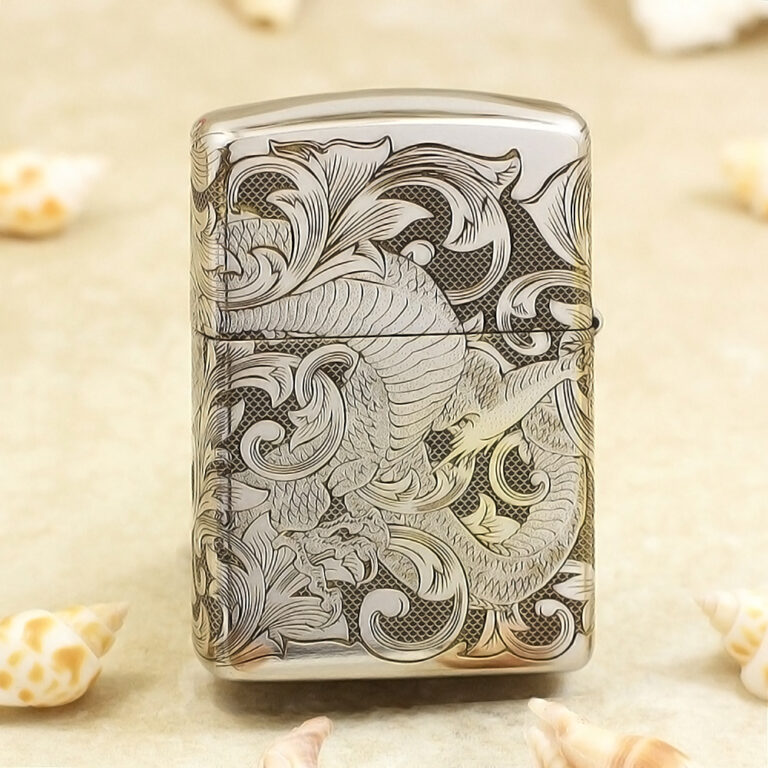 Silver lighter with an intricate dragon and swirling floral engravings on the front, shell-colored background nearby.