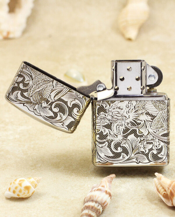 KZ143-02 Ornate engraved lighter on sandy beach with seashells nearby, lid open.