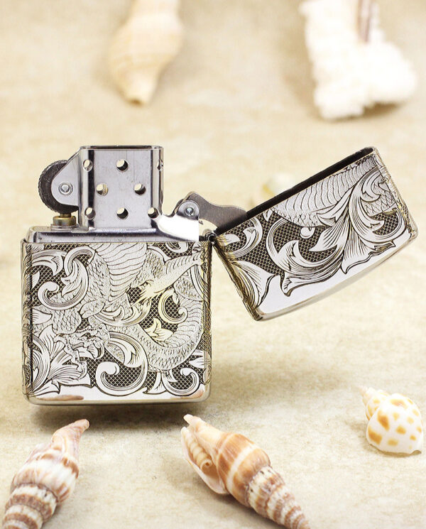 KZ143-03 Metal Zippo-style lighter with intricate black-and-white floral engravings, open lid, on a sandy beach with seashells nearby.