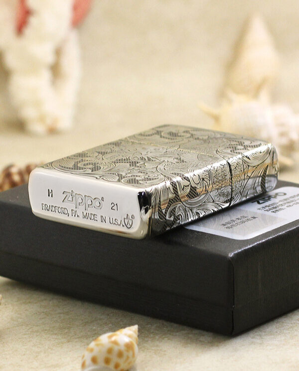 KZ143-05 Engraved Zippo lighter with intricate patterns rests on a black box.