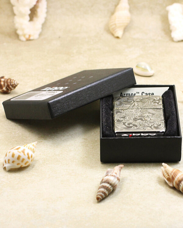 KZ143-06 Open black box showing a silver engraved lighter on a foam insert, surrounded by seashells on sand.