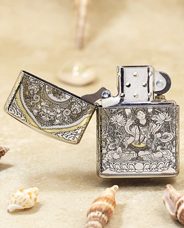 KZ144-02 Ornate metal lighter with intricate engravings, open lid, placed on a sandy surface with seashells nearby.