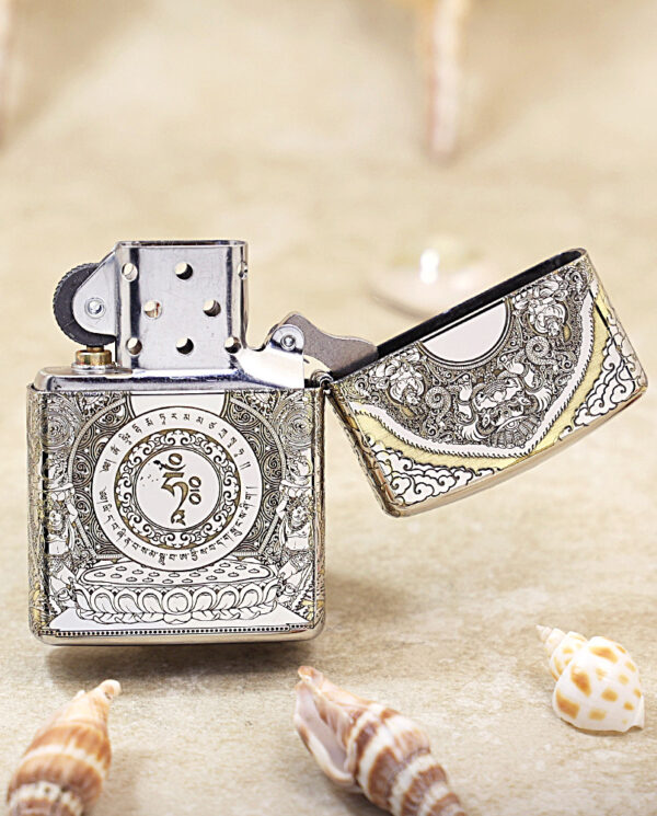 KZ144-03 Ornate metal lighter with detailed engravings, open lid, resting on a sandy surface with seashells nearby.