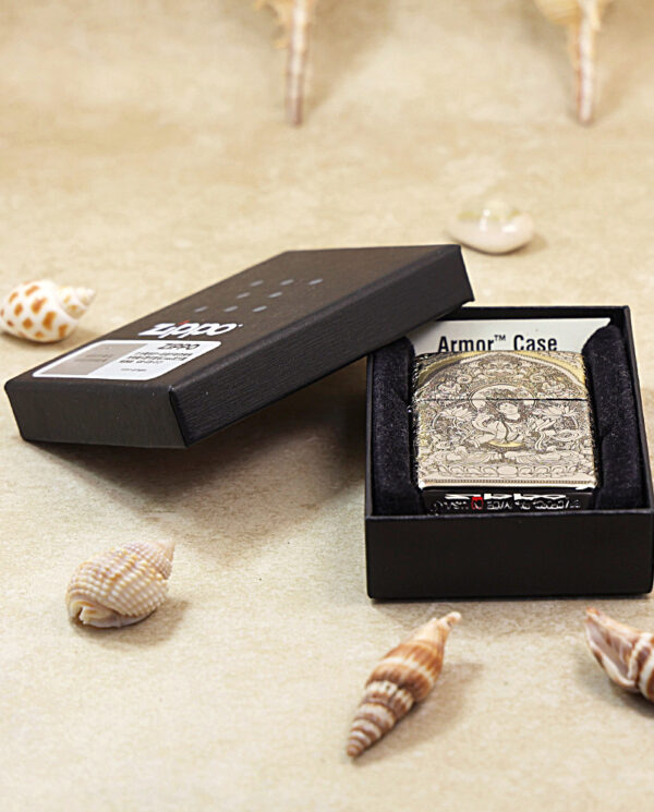 KZ144-06 Engraved Zippo-style lighter case in a black presentation box on a sandy surface with seashells nearby.