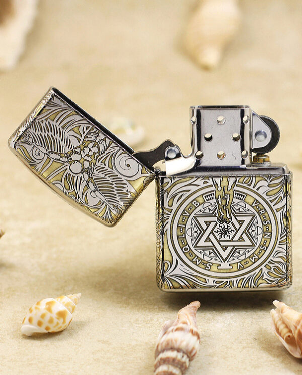 KZ145-02 Metal lighter with intricate geometric and floral engravings, lid open, resting on sandy surface among seashells