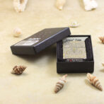 Open black box revealing an ornate, gold-patterned card labeled 'Armor Case' on a sandy surface with seashells nearby, inner velvet lining visible