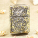 Metal lighter with an intricate dragon engraving in dark lines on a gold-tone surface.