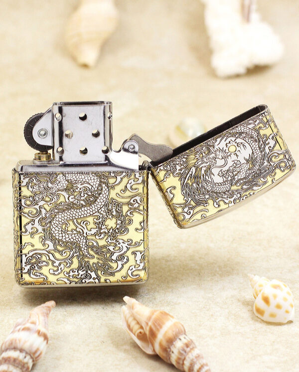 KZ146-03 Open, dragon-engraved metal lighter resting on sand among seashells.