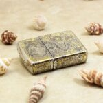 Chinese dragon engraved Zippo Armor lighter lying flat among seashells