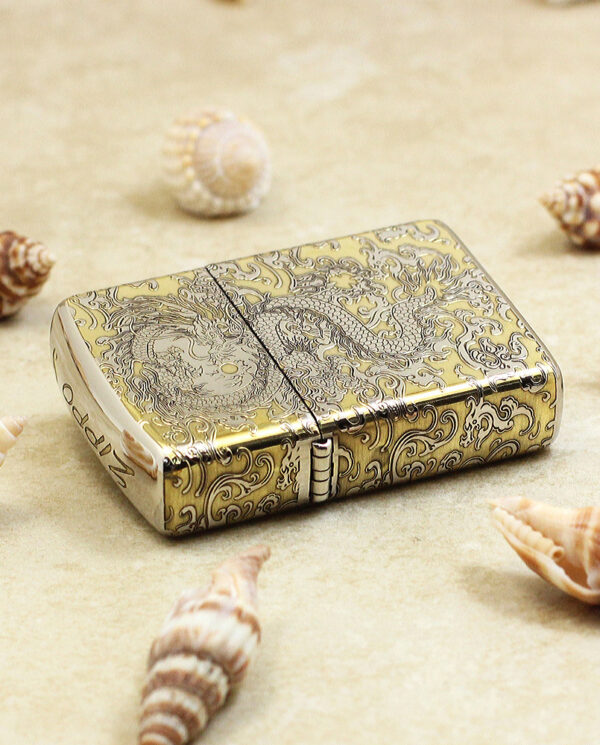 KZ146-04 Ornate gold pocket lighter with intricate engravings on a sandy surface among seashells
