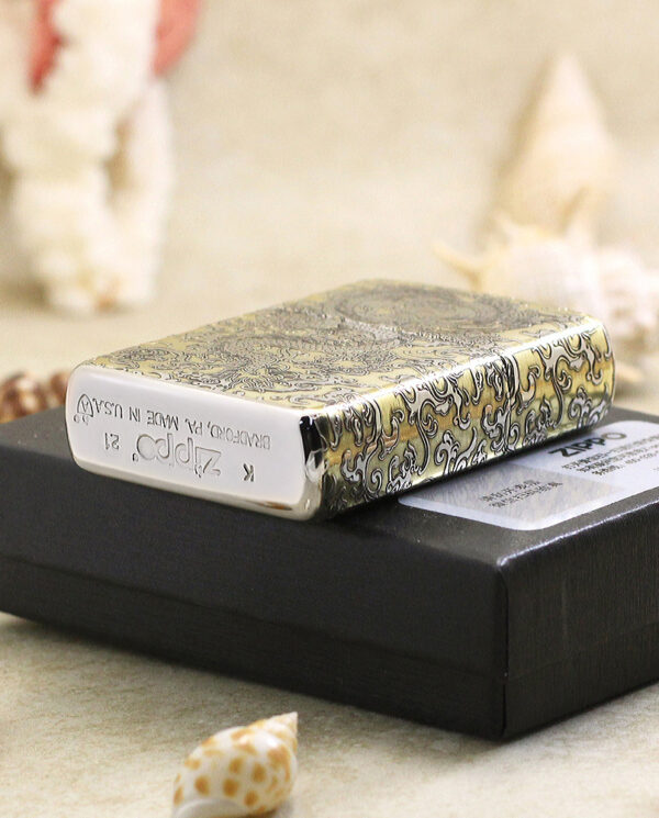 KZ146-05 Decorative metal lighter with an intricate swirling pattern resting on a black box, with seashells in the background.