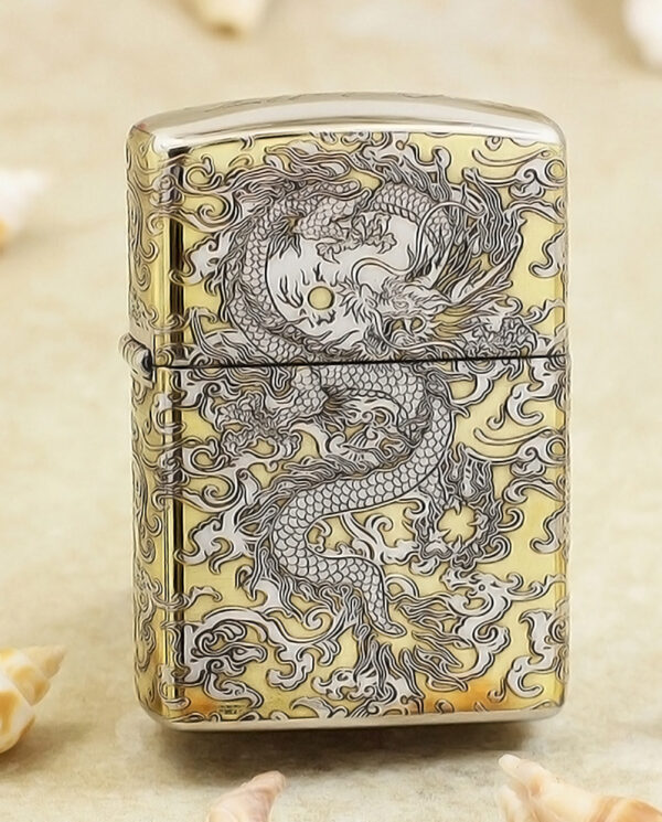 KZ146 Gold-toned metal lighter with intricate black dragon design across front and sides, standing on a sandy surface with seashells nearby.