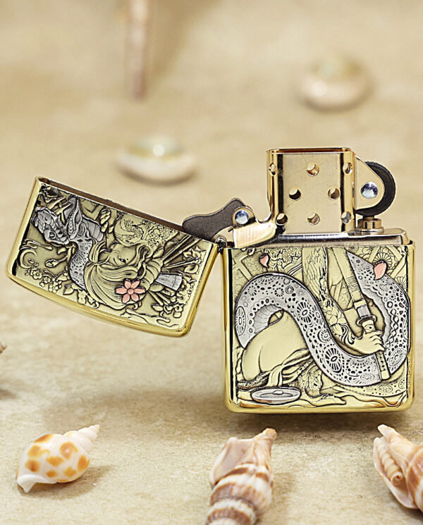 Gold Zippo lighter with intricate dragon and floral engravings, lid open, placed on sandy surface among seashells.