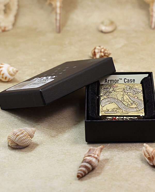Gold-toned Zippo lighter with a dragon engraving in a black Armor Case box on a sandy surface.