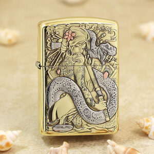 Gold Zippo-style lighter with an intricate engraving of a woman and a coiling dragon among flowers, set on a sandy background with seashells nearby.