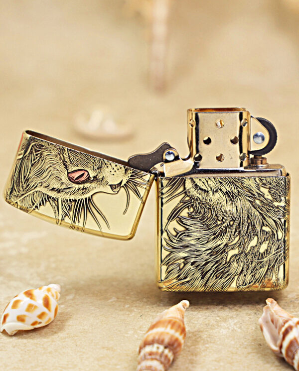 KZ152-02 Gold Zippo lighter with a wolf engraving, lid open, resting on sandy beach with seashells nearby.