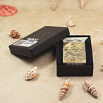 Gold Zippo lighter with a rabbit engraving inside a black box labeled Armor Case, resting on a sandy beach with seashells nearby