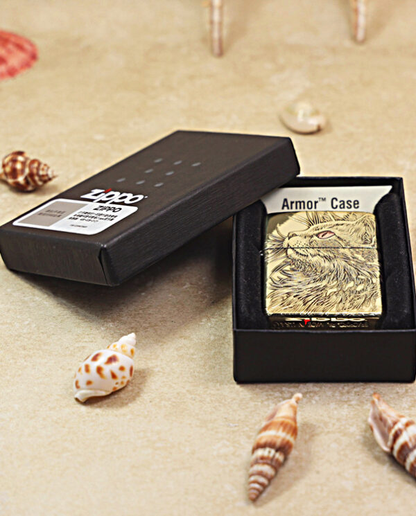 KZ152-06 Gold Zippo lighter with a rabbit engraving inside a black box labeled Armor Case, resting on a sandy beach with seashells nearby