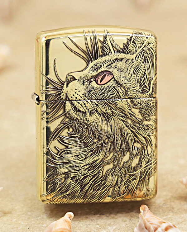 KZ152 Gold Zippo lighter with a detailed cat engraving on the front, resting on sandy beach with seashells nearby