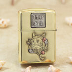 Gold metal lighter with Chinese characters on the top and a carved cat surrounded by flowers on the front (decorative engraving).