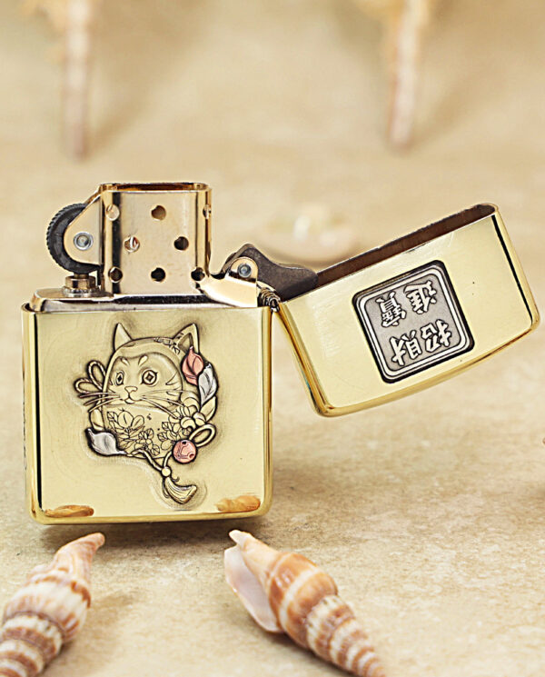 Gold Zippo lighter with a cute cat and flowers engraving, lid open, surrounded by seashells
