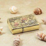 Gold decorative lighter with ornate engravings and a dragon motif, placed on sand with seashells nearby.