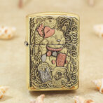 Gold Zippo lighter with an embossed Maneki-neko (lucky cat) design and hanging charms, ornate and decorative.