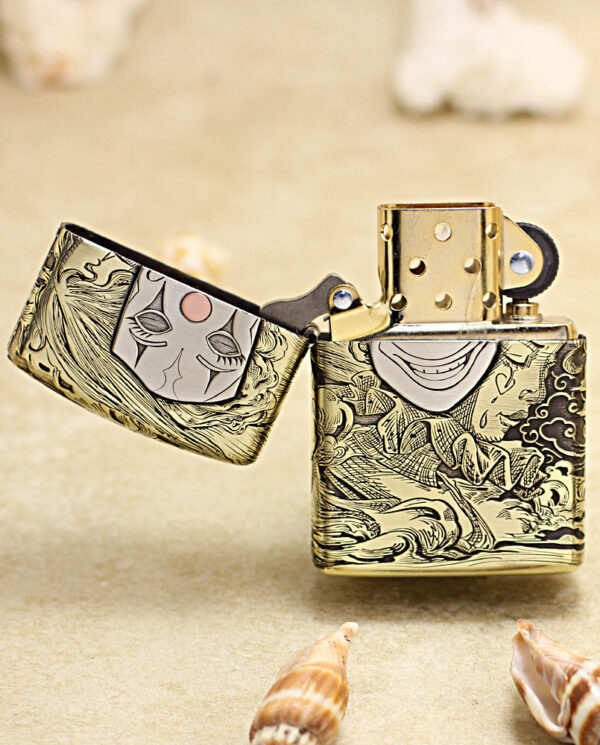 KZ154-02 Gold Zippo lighter with ornate engraving and open lid, featuring a stylized face and waves on a sandy background.