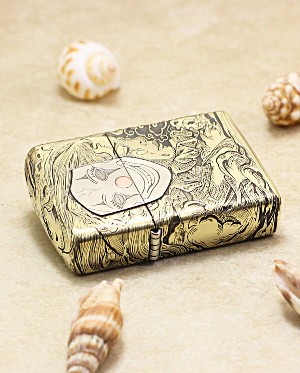 KZ154-04 Ornate gold-tone lighter with a detailed engraving of a face, placed on sand among seashells.