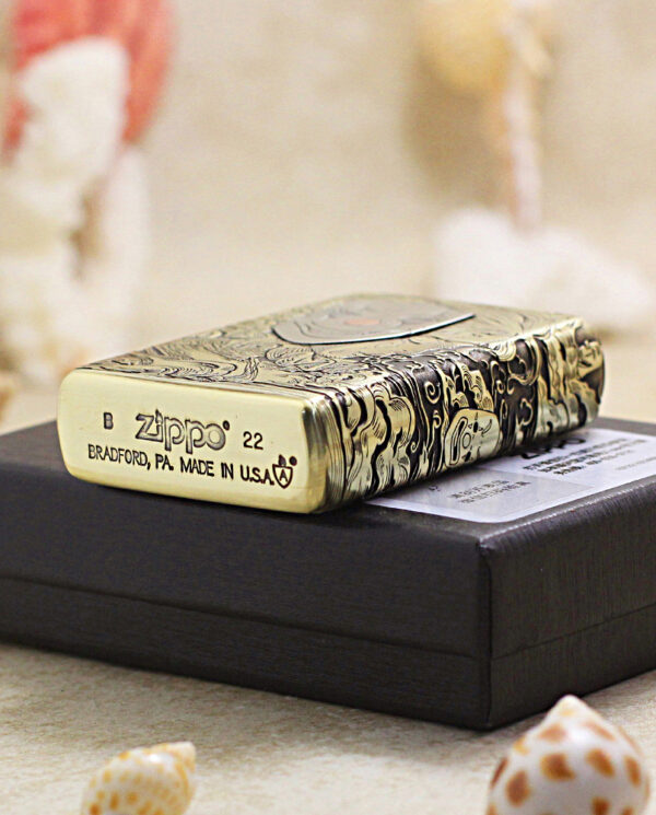 KZ154-05 Metal Zippo lighter with intricate engraving rests on a black box; shows 'Zippo' and 'Bradford, PA Made in USA' engraved on the base, 22.