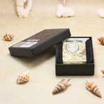 Gold engraved lighter in a black open jewelry box on a sandy surface, surrounded by seashells (beach-themed product photo).