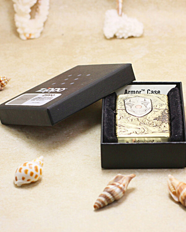 KZ154-06 Gold engraved lighter in a black open jewelry box on a sandy surface, surrounded by seashells (beach-themed product photo).